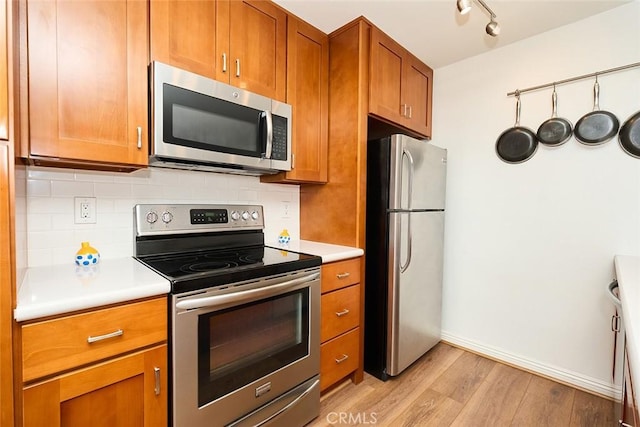 kitchen with decorative backsplash, light hardwood / wood-style flooring, rail lighting, and appliances with stainless steel finishes