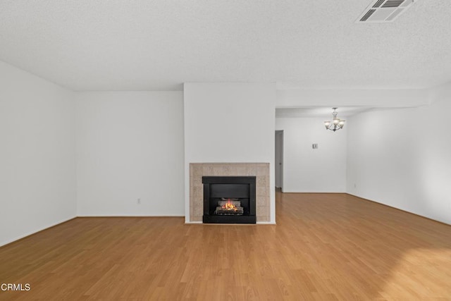 unfurnished living room featuring a textured ceiling, a tile fireplace, light hardwood / wood-style flooring, and a notable chandelier