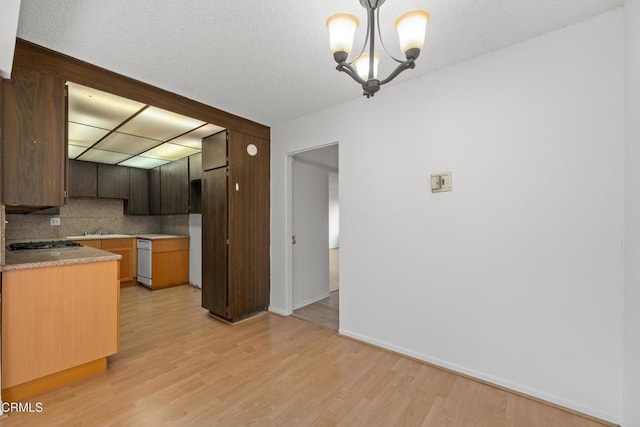 kitchen featuring decorative light fixtures, stainless steel gas stovetop, decorative backsplash, a notable chandelier, and light hardwood / wood-style flooring