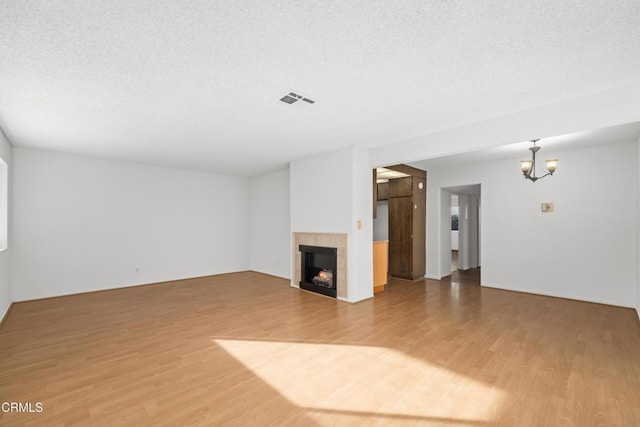 unfurnished living room with wood-type flooring, a textured ceiling, a notable chandelier, and a fireplace