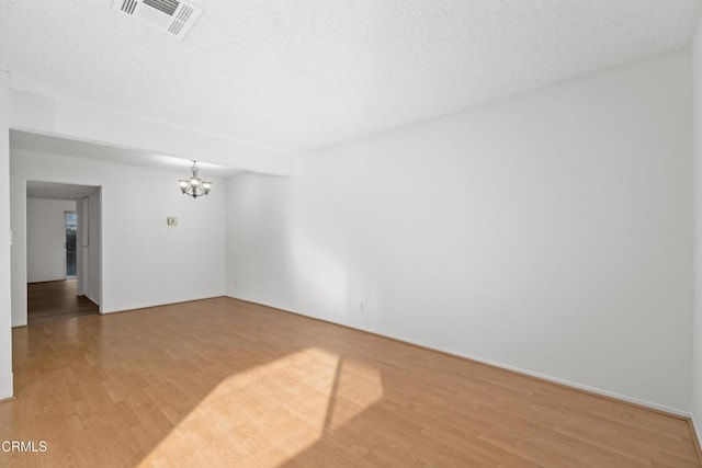 unfurnished room featuring an inviting chandelier, hardwood / wood-style floors, and a textured ceiling