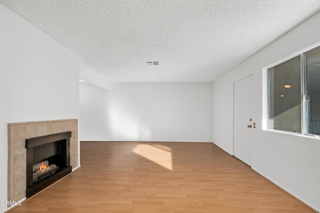 unfurnished living room with a textured ceiling, a tile fireplace, and light wood-type flooring