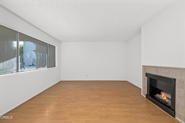 unfurnished living room with a tile fireplace, a textured ceiling, and light wood-type flooring