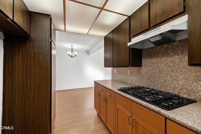 kitchen with black gas cooktop, light wood-type flooring, decorative backsplash, hanging light fixtures, and an inviting chandelier