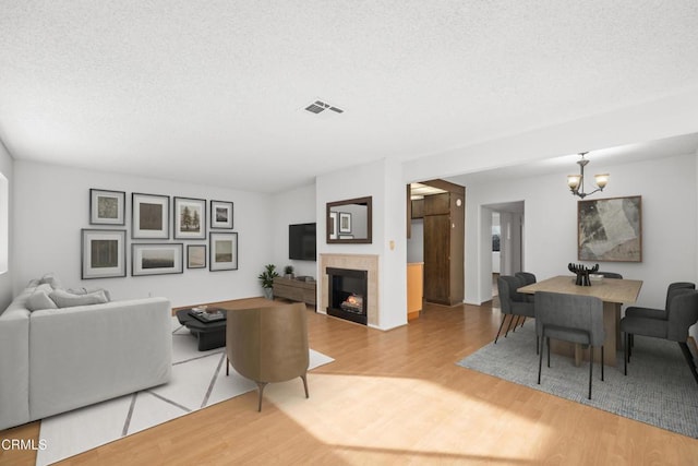 living room featuring a textured ceiling, a fireplace, wood finished floors, visible vents, and an inviting chandelier