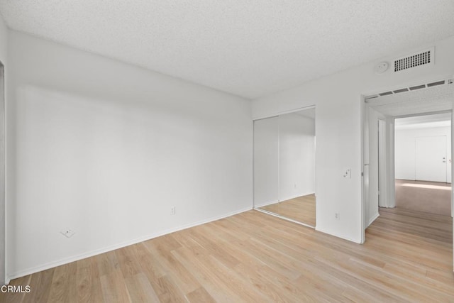 unfurnished bedroom featuring light wood-style floors, a textured ceiling, visible vents, and a closet