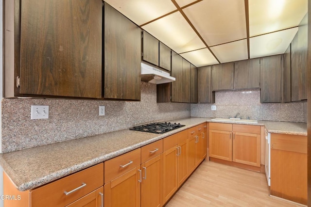 kitchen with light wood finished floors, black gas cooktop, light countertops, a sink, and under cabinet range hood