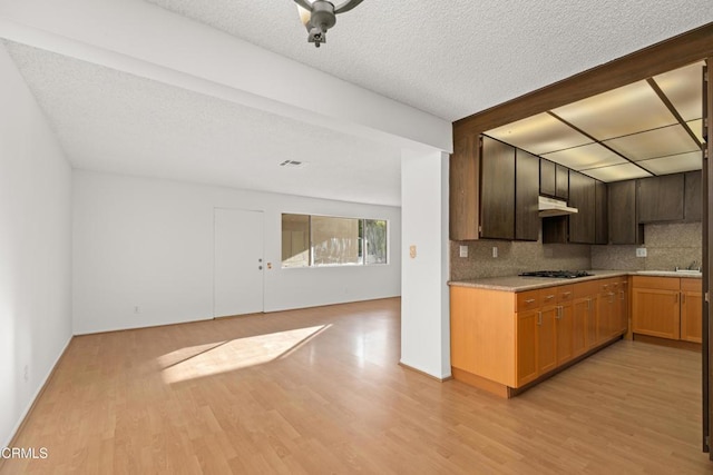 kitchen with tasteful backsplash, light wood-style flooring, black gas cooktop, light countertops, and under cabinet range hood