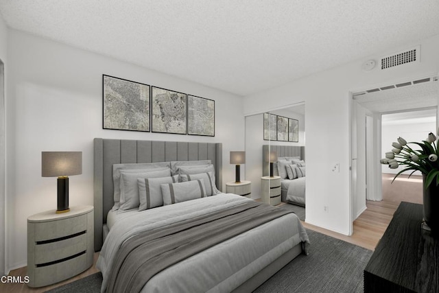 bedroom featuring visible vents, a textured ceiling, baseboards, and wood finished floors