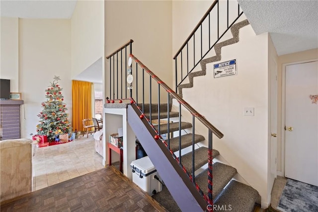 staircase featuring a towering ceiling, parquet flooring, and a textured ceiling