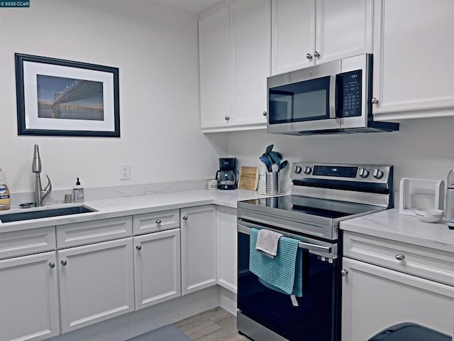 kitchen featuring appliances with stainless steel finishes, white cabinetry, sink, light hardwood / wood-style floors, and light stone countertops