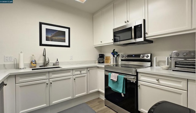 kitchen with sink, light hardwood / wood-style flooring, stainless steel appliances, light stone countertops, and white cabinets