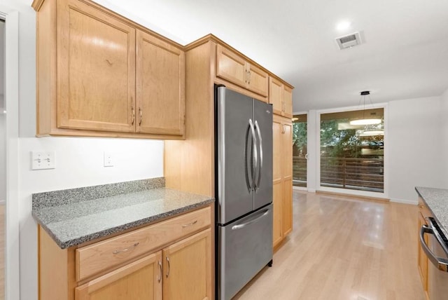 kitchen featuring pendant lighting, appliances with stainless steel finishes, dark stone countertops, light brown cabinetry, and light wood-type flooring