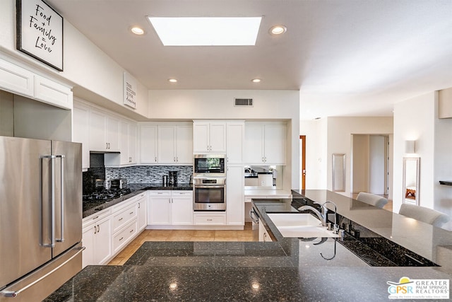 kitchen with appliances with stainless steel finishes, sink, dark stone countertops, and white cabinets