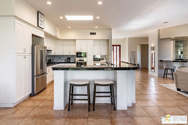 kitchen featuring appliances with stainless steel finishes, tasteful backsplash, white cabinets, a kitchen bar, and a center island