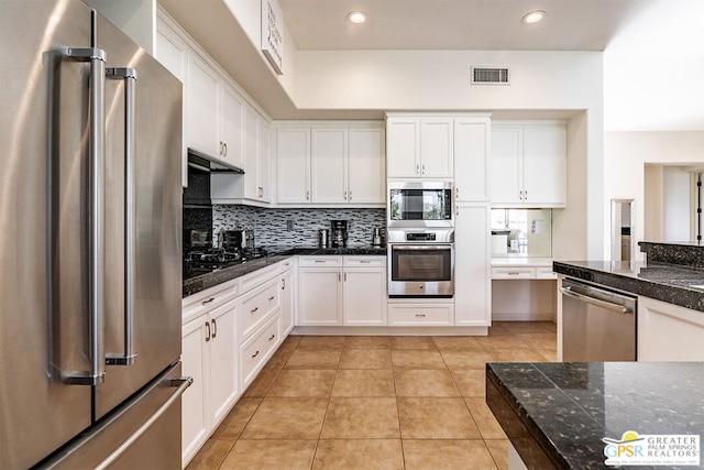 kitchen featuring light tile patterned flooring, tasteful backsplash, dark stone countertops, appliances with stainless steel finishes, and white cabinets