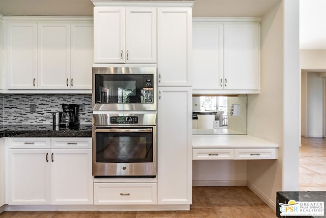 kitchen featuring white cabinetry, dark stone countertops, tasteful backsplash, built in microwave, and oven