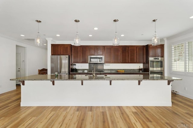 kitchen with stainless steel appliances, pendant lighting, a kitchen breakfast bar, and light hardwood / wood-style flooring