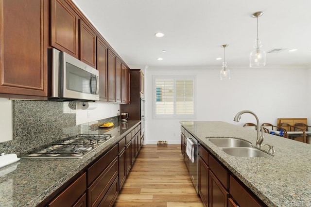 kitchen featuring sink, pendant lighting, stainless steel appliances, light stone countertops, and light hardwood / wood-style floors