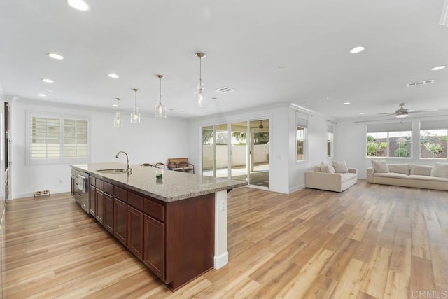 kitchen with sink, light hardwood / wood-style flooring, light stone countertops, an island with sink, and decorative light fixtures