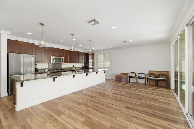 kitchen with stainless steel appliances, hanging light fixtures, a kitchen breakfast bar, and light hardwood / wood-style floors