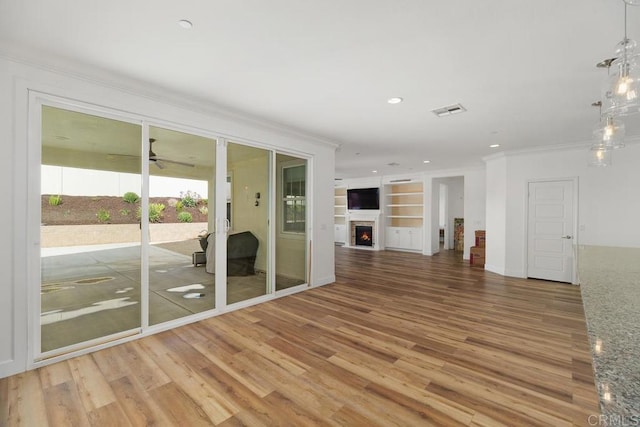 unfurnished living room featuring hardwood / wood-style floors, crown molding, built in features, and ceiling fan