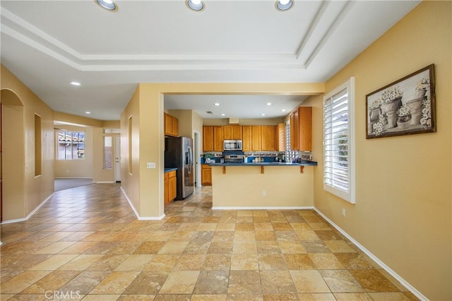 kitchen featuring stainless steel appliances, a raised ceiling, a kitchen bar, and kitchen peninsula