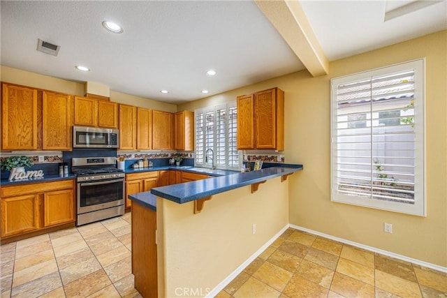 kitchen with appliances with stainless steel finishes, beamed ceiling, sink, a kitchen breakfast bar, and kitchen peninsula