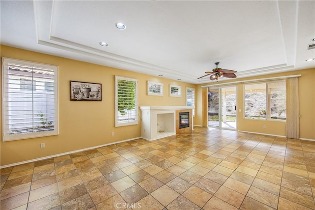 unfurnished living room featuring ceiling fan, a raised ceiling, and a healthy amount of sunlight