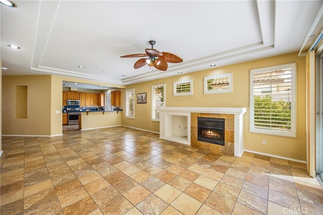 unfurnished living room featuring ceiling fan, a fireplace, and a raised ceiling