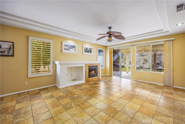 unfurnished living room with ceiling fan, a fireplace, and a tray ceiling