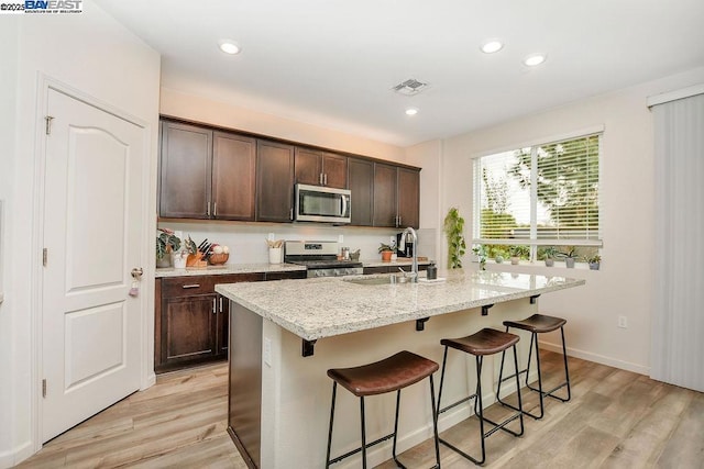 kitchen with appliances with stainless steel finishes, sink, a kitchen island with sink, and dark brown cabinetry