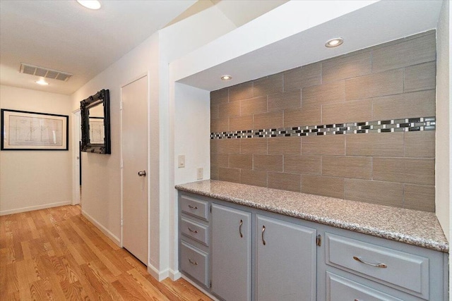 interior space featuring tasteful backsplash, light stone countertops, light hardwood / wood-style flooring, and gray cabinetry