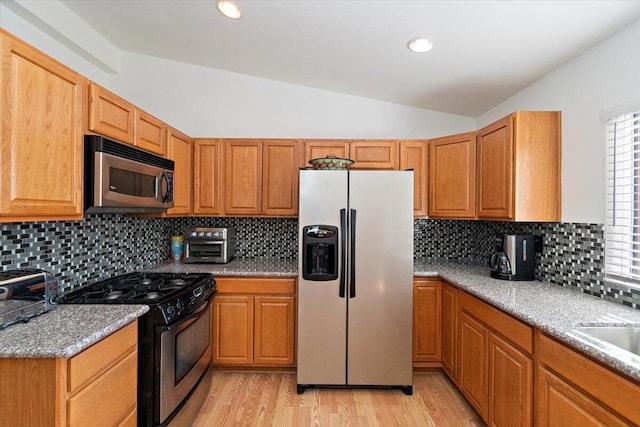 kitchen featuring vaulted ceiling, appliances with stainless steel finishes, tasteful backsplash, light stone countertops, and light wood-type flooring