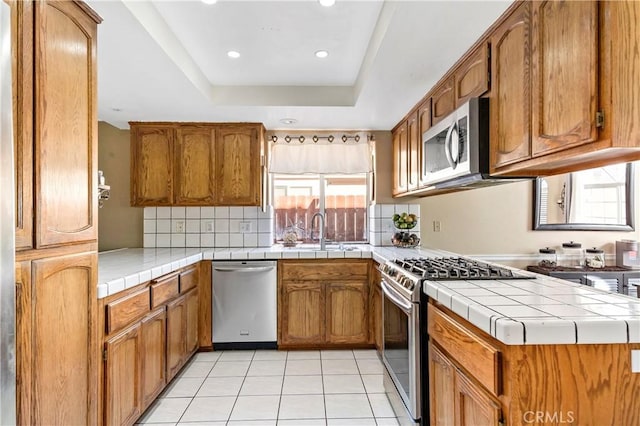 kitchen featuring sink, backsplash, stainless steel appliances, tile countertops, and a raised ceiling