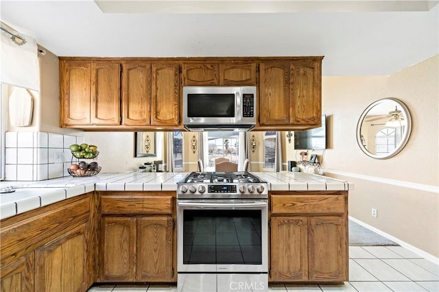 kitchen with light tile patterned flooring, appliances with stainless steel finishes, tile countertops, backsplash, and kitchen peninsula