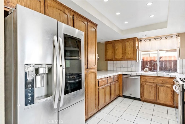 kitchen featuring appliances with stainless steel finishes, tile countertops, backsplash, light tile patterned floors, and a raised ceiling