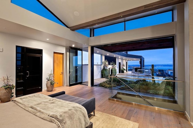 bedroom with a water view, wood-type flooring, and high vaulted ceiling