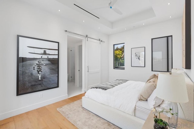 bedroom featuring a raised ceiling, a barn door, hardwood / wood-style floors, and ceiling fan