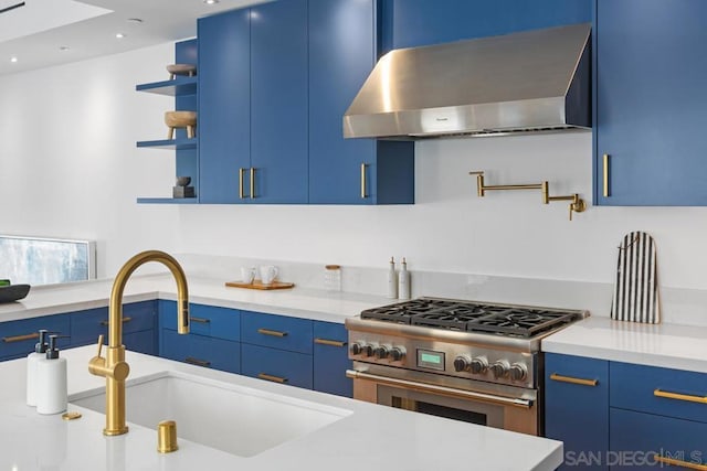 kitchen with blue cabinets, sink, wall chimney range hood, and stainless steel range