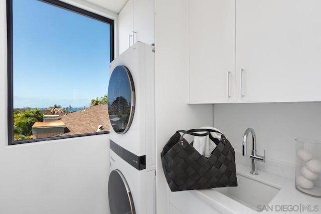 clothes washing area featuring sink, a wealth of natural light, cabinets, and stacked washer / dryer