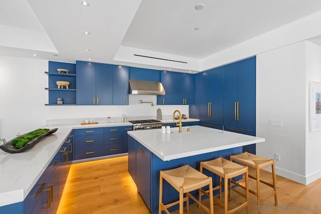 kitchen featuring a kitchen island with sink, blue cabinetry, exhaust hood, and a breakfast bar