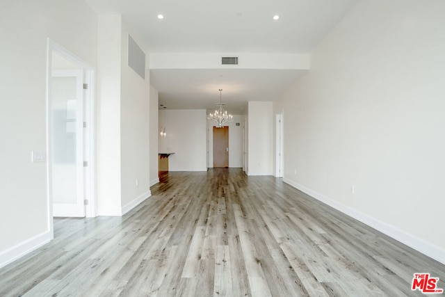 unfurnished living room featuring a chandelier and light wood-type flooring