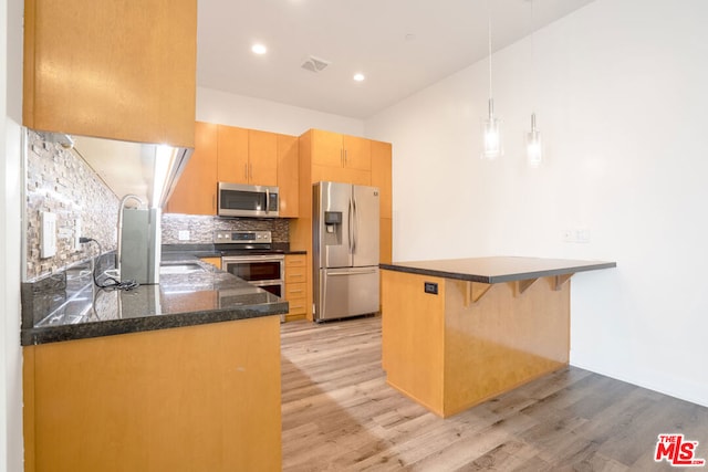 kitchen featuring hanging light fixtures, light wood-type flooring, kitchen peninsula, stainless steel appliances, and backsplash