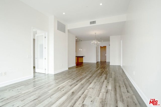 empty room with light hardwood / wood-style flooring and a notable chandelier