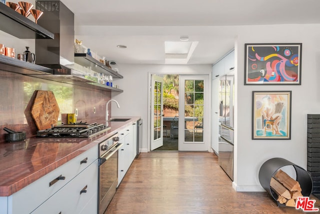 bar featuring appliances with stainless steel finishes, sink, backsplash, white cabinets, and light hardwood / wood-style floors