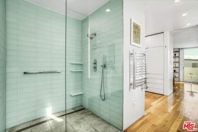 bathroom featuring a tile shower, radiator heating unit, and wood-type flooring