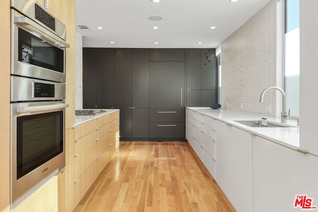 kitchen with sink, light brown cabinets, backsplash, and light hardwood / wood-style flooring