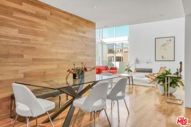 dining space featuring floor to ceiling windows, light wood-type flooring, and wood walls