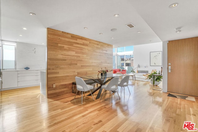 dining room featuring light hardwood / wood-style flooring, a wall of windows, and wood walls